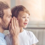 Dad whispering a secret into little boy's ear