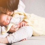 Little girl holding newborn baby and kissing forehead