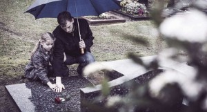 Girl and man putting flowers on a grave in the rain