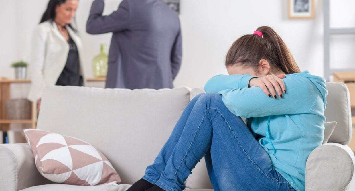 teen girl crying on couch with parents fighting
