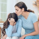 mom kissing tween daughter on forehead