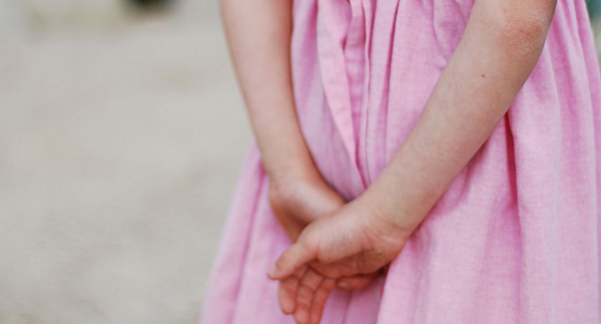 girl in pink dress, clasping hand behind her.