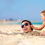 Dad buried in sand with child holding up a phone to his ear