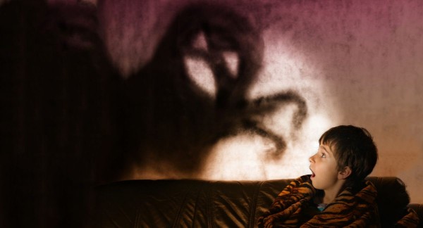 A shadow monster on the wall with a child scared in bed
