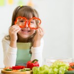 Young girl holding bell pepper slices over her eyes as glasses