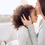 Mom kissing young daughter on the forehead