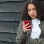 Sad mixed race girl texting on phone